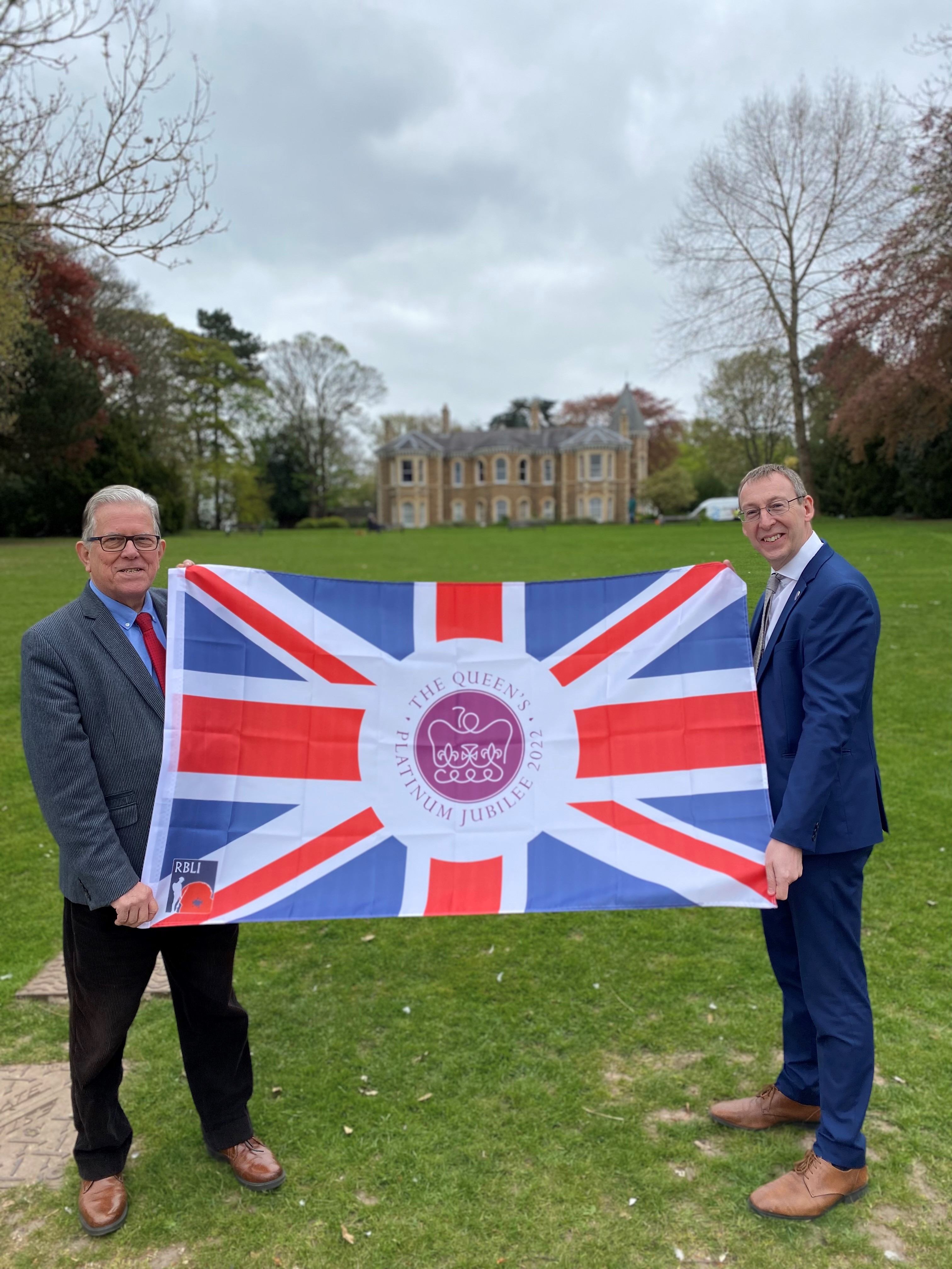 John and Mike standing with a flag outside arnot hill house